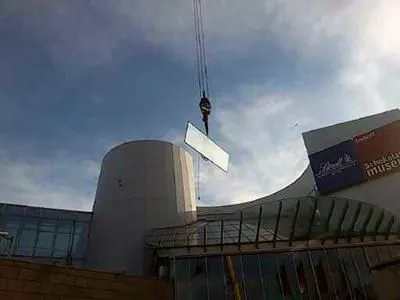 Ein Kran hebt ein großes Stück Glas vor ein Gebäude.