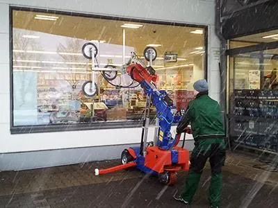 Ein Mann hebt mit einer Maschine ein Glasfenster aus dem Schnee an.